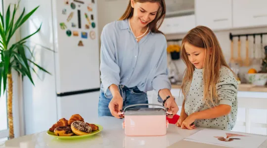 Cheerful woman closes the lunch box and prepares her daughter for school | Merry Maids