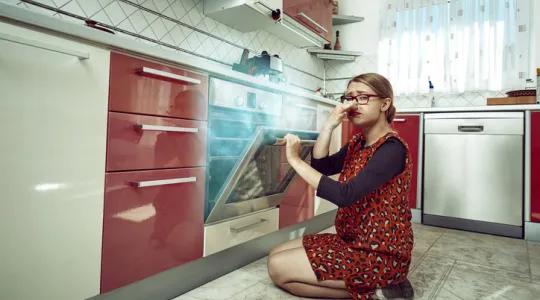 Young woman inside her kitchen opening the stove, burning food inside it, negative expression | Merry Maids