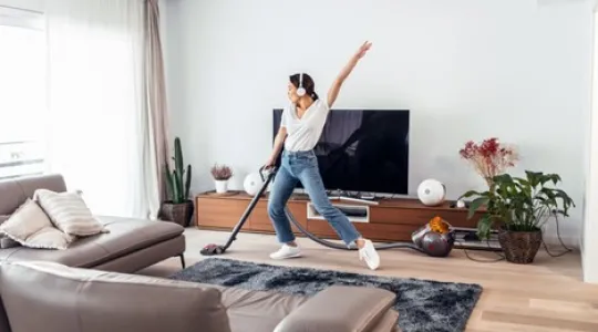 Young woman listening to music and dancing around the living room while vacuuming. She is having fun while tidying up her home. | Merry Maids®