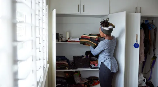 Woman putting folded clothes away in the closet to organize her space. | Merry Maids®