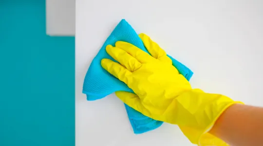 Female hand in yellow rubber gloves wipes a modern white kitchen with a microfiber cloth. | Merry Maids