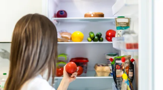 Young pretty woman taking fresh healthy tomato vegetables from refrigerator | Merry Maids