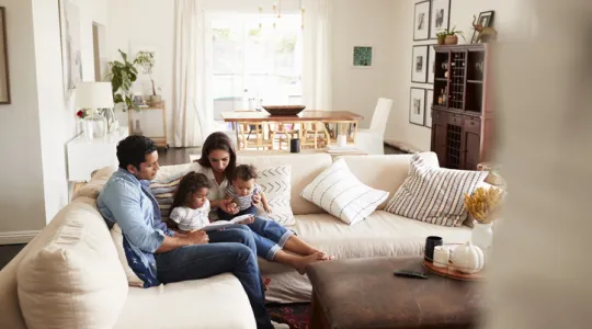 Family of four reading a book on the couch in a clean and tidy living room. | Merry Maids®