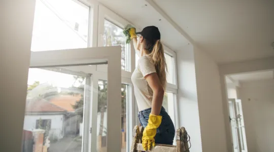 Woman on ladder in yellow gloves cleaning window with rag | Merry Maids