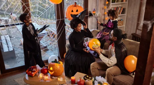 Happy African American family in costumes talking during a Halloween celebration at home | Merry Maids