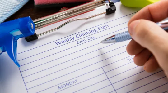 Close-up Of Person Hand Filling Weekly Cleaning Plan Form | Merry Maids
