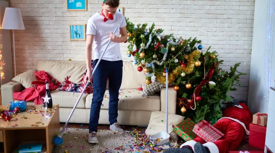 Young man wearing and surrounded by Christmas themed decorations cleaning up after the new year. | Merry Maids®