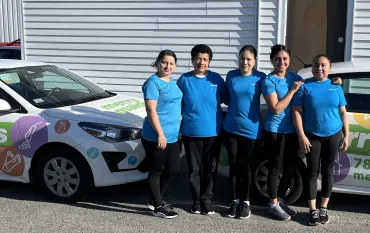 House cleaning team from Merry Maids standing in front of a branded company car outside a building in Arlington, ready to provide professional home cleaning services.