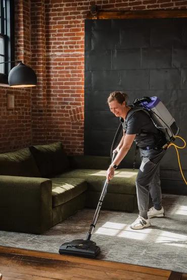 Merry Maids of York technician using a ProTeam backpack vacuum to clean a living room carpet