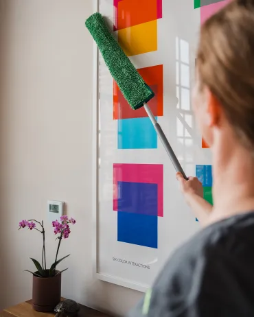 Merry Maids of York cleaning technician dusting wall art in a client's living room
